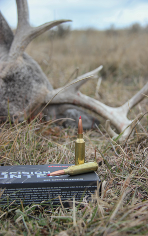 Two 6.5 PRC cartridges on top of box, with downed buck in background