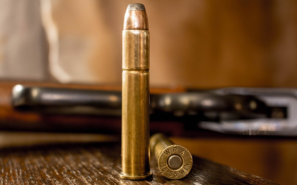 Two rounds of .38-55 Winchester ammunition on wood table.