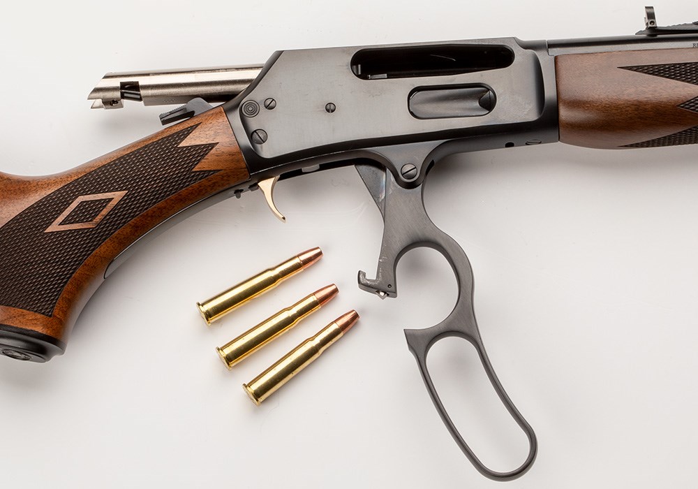 Marlin Model 336 Classic with lever action open and three rounds of .30-30 Winchester ammunition laying near the grip.