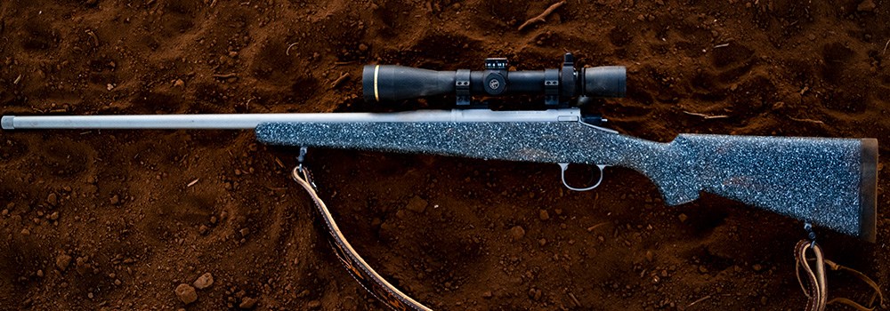 Nosler Model 21 rifle topped with Leupold VX-6HD riflescope and Leupold Custom Dial System turret resting on red clay dirt.