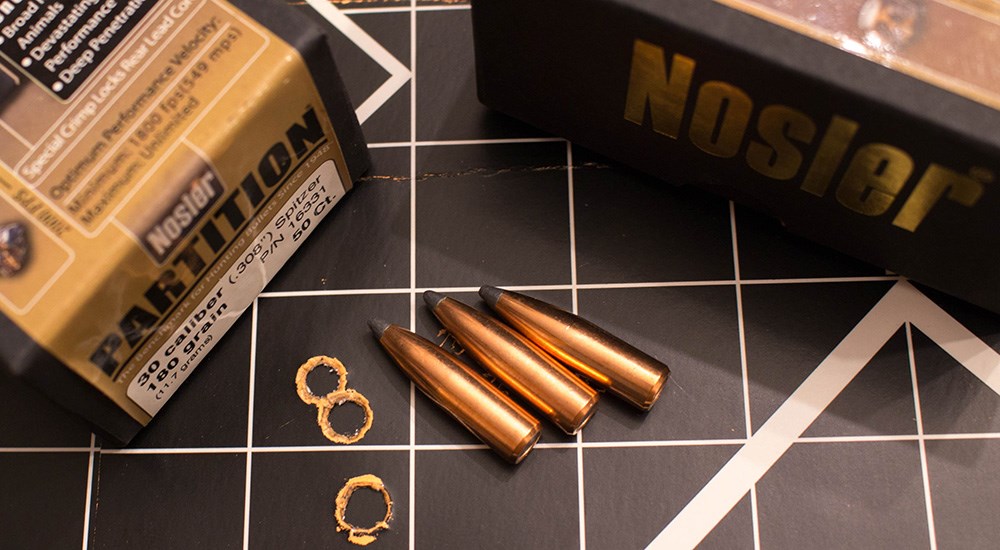Nosler Partition bullets laying next to three touching holes on paper shooting target.