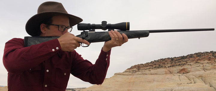 Man shoots a scoped rifle offhand in the desert