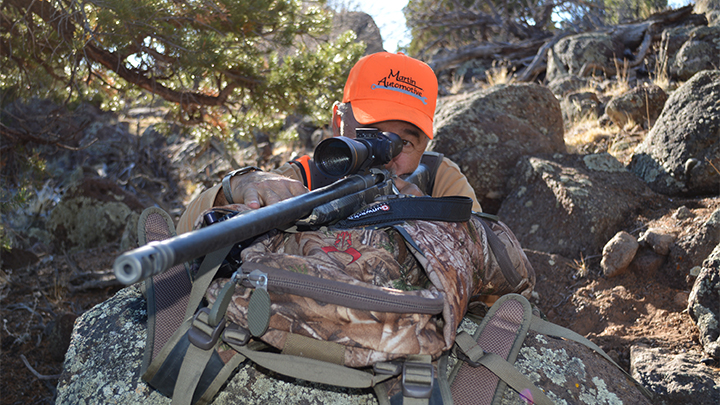 Hunter resting rifle across hunting pack, preparing to take a shot