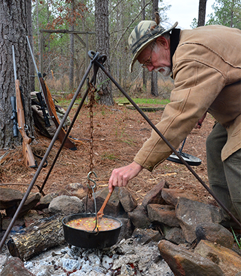 Man cooking soup in cast iron pot over camp fire
