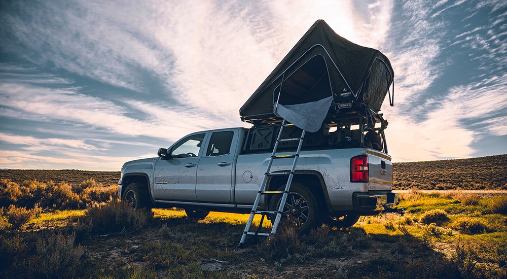 GMC truck in open field with rooftop tent over rack storage system.