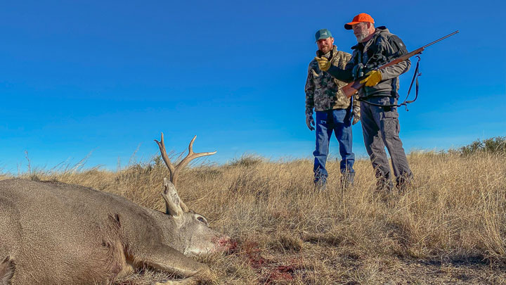 Hunters standing over a fallen mule deer on the wide-open plains