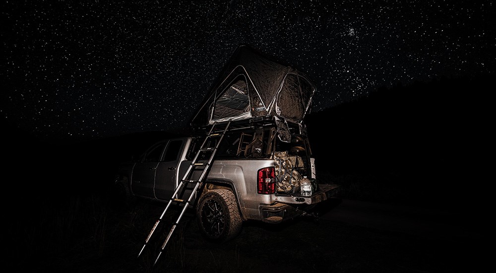 Truck bed rooftop hard shell tent in darkness with starry sky.