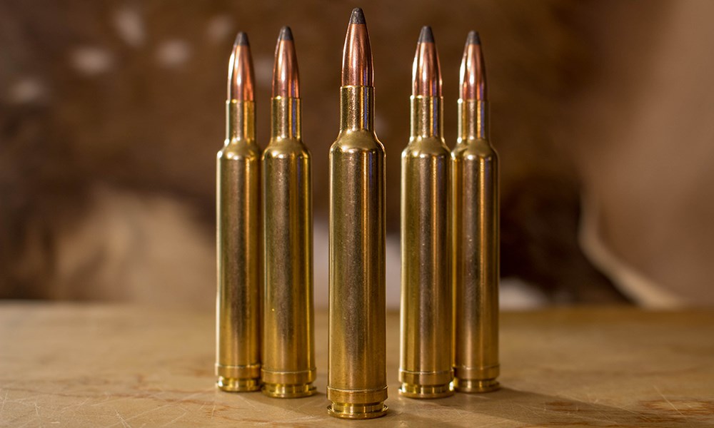 Five .240 Weatherby Magnum ammunition rounds standing on wood table in triangle formation.