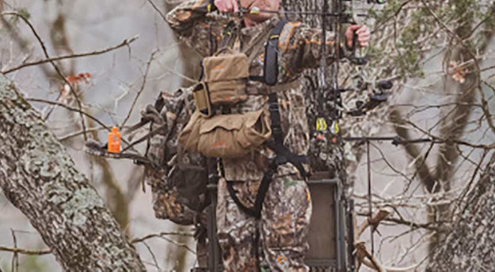 Bowhunter standing on tree stand drawing back compound bow.
