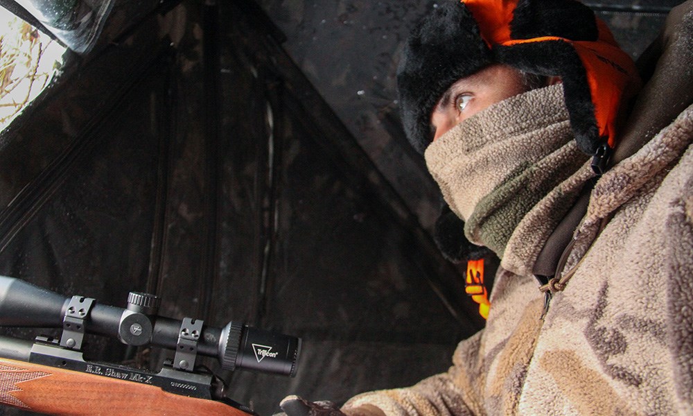 Deer hunting in ground blind with face mask on.