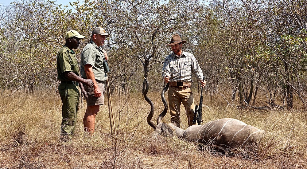 Three male hunters viewing kudu in South African terrain