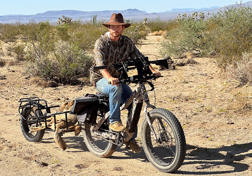 Male hunter riding QuietKat e-bike with coyote in trailer.