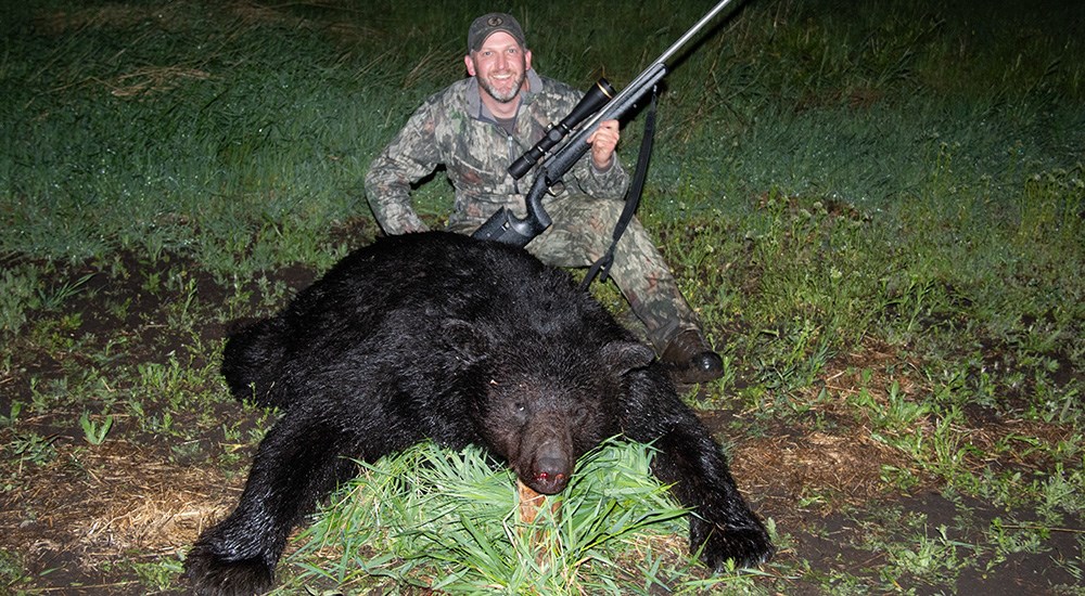 Hunter posing with black bear on grass.
