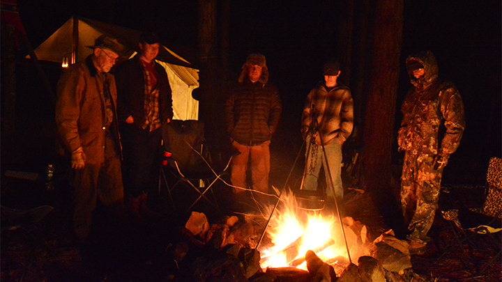 Men cooking in dutch oven over camp fire