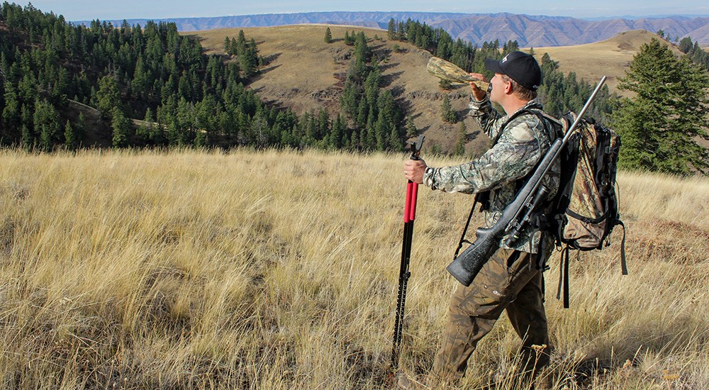 Elk hunter standing on mountain using bugle elk call.